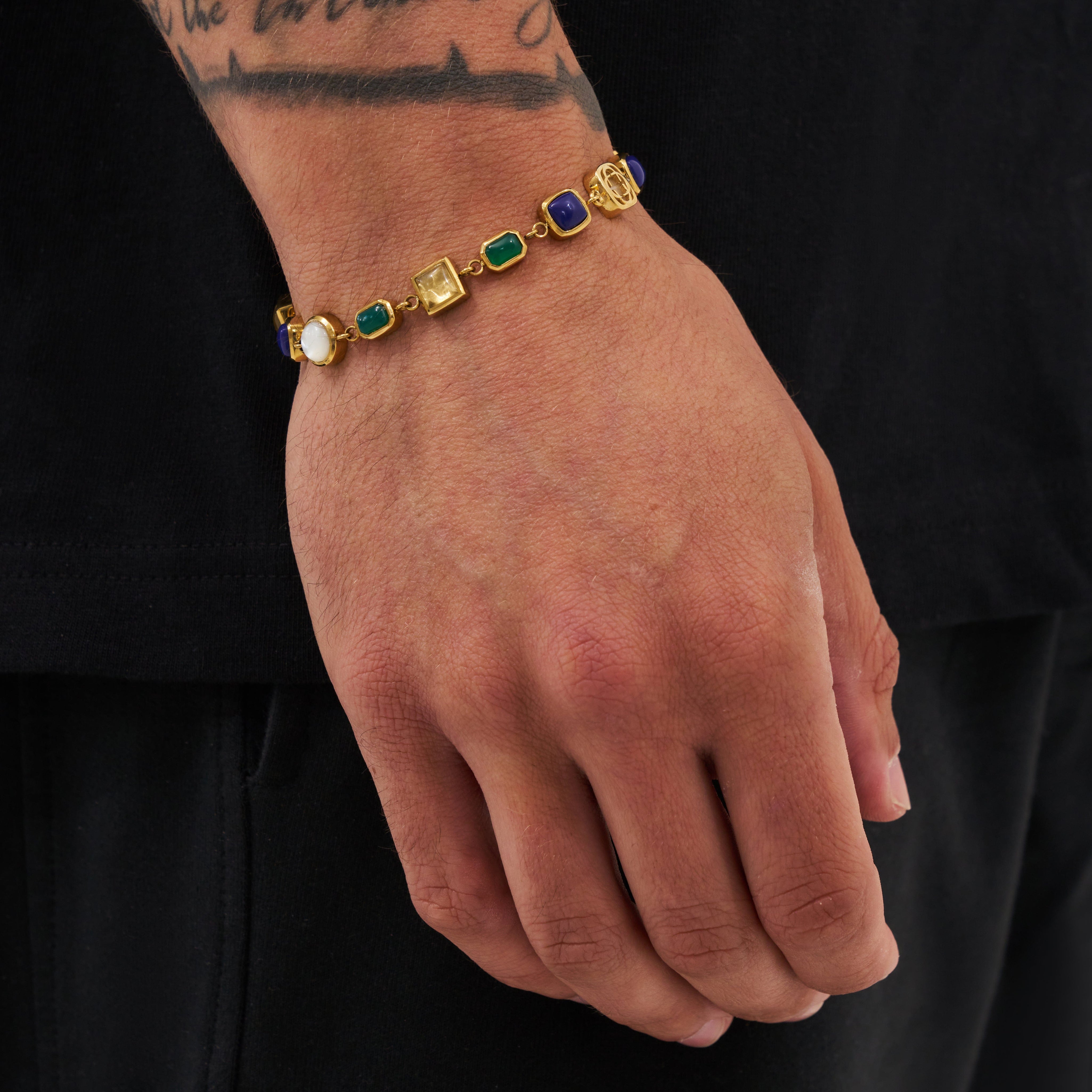 Gold bracelet with colored stones on a wrist against a black background
