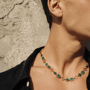 Necklace with green gemstones worn by a person against a textured wall.