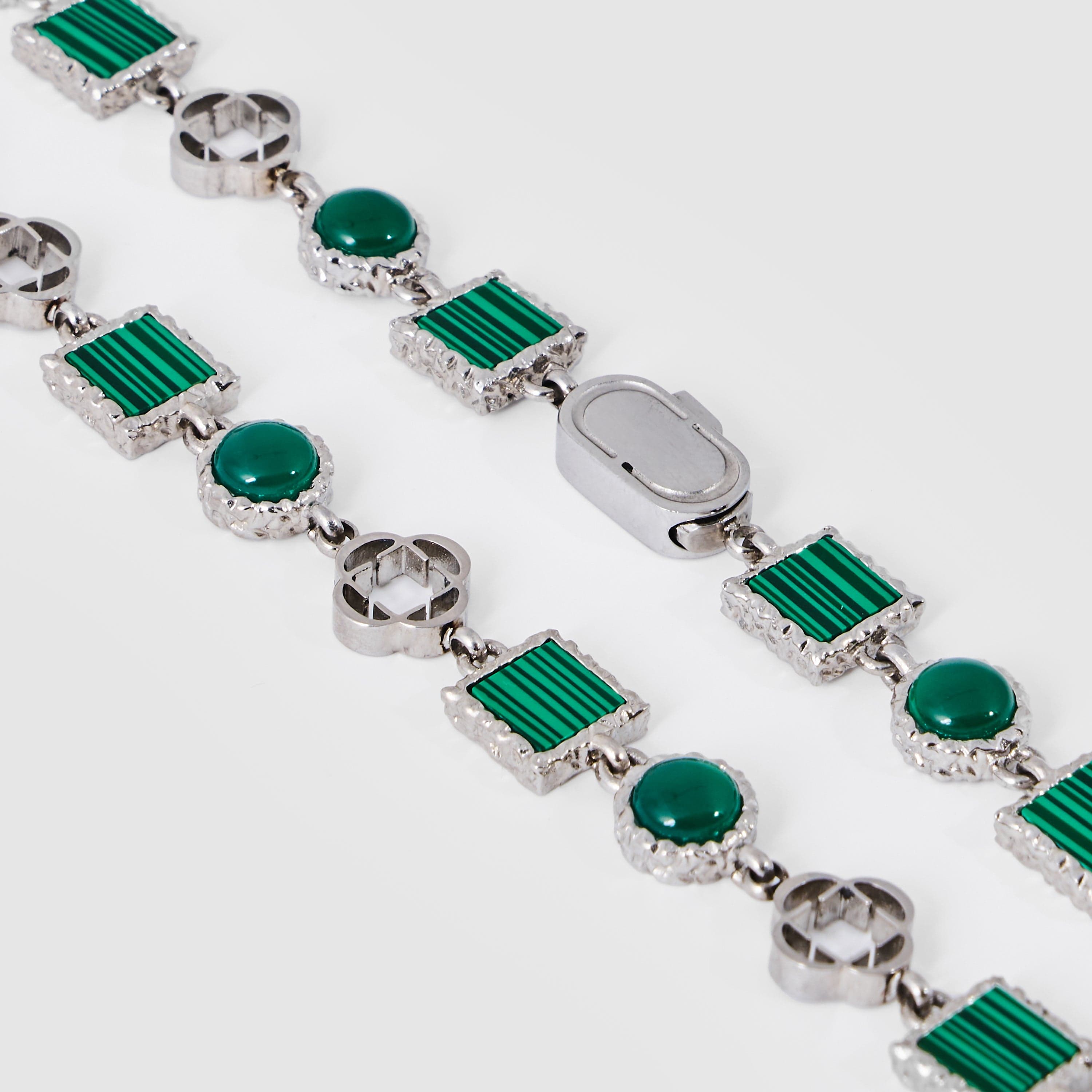 Silver bracelet with green gemstones on a white background